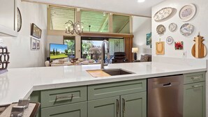A modern kitchen with a large island, green cabinets, and a stainless steel dishwasher. - Newly Remodeled!! 2BR, Pools & hot tubs, Golf View (Waikoloa Village)
