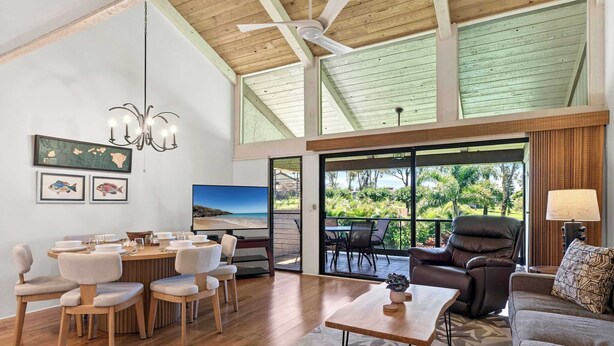 A spacious living area with a dining table, chairs, a sofa, a coffee table, a fireplace, and a large window with a view of greenery. - Newly Remodeled!! 2BR, Pools & hot tubs, Golf View (Waikoloa Village)