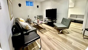 Una sala de estar moderna con un sofá, una mesita de centro y un televisor. Hay una ventana con cortinas azules y un espejo en la pared.