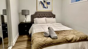 Un dormitorio con cama, mesita de noche, lámpara y una obra de arte enmarcada en la pared.