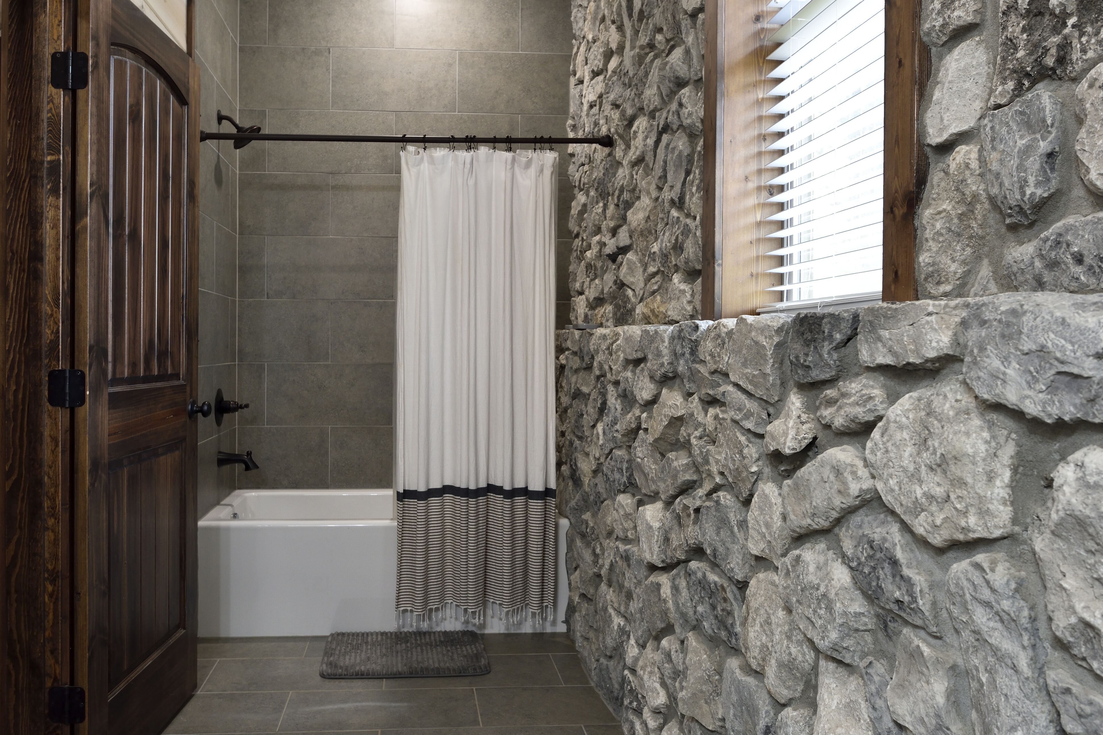 A bathroom with a stone wall, a bathtub, and a shower curtain.