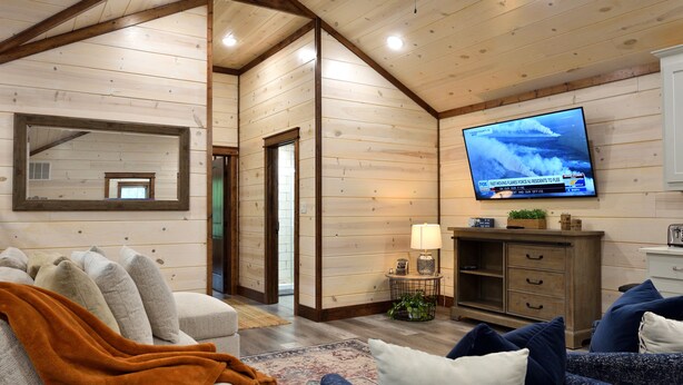 A cozy living room with a television mounted on the wall, a sofa with a throw blanket, and a coffee table.