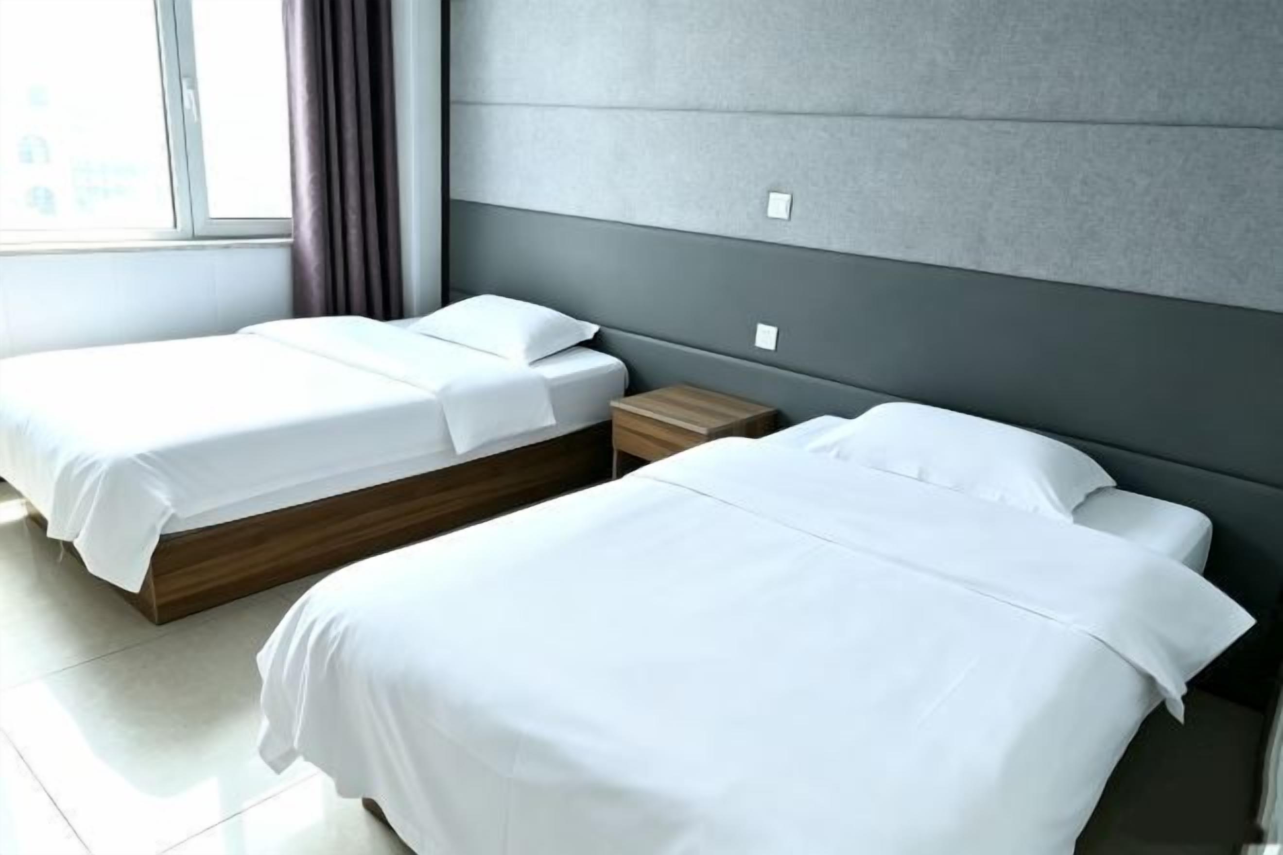 A hotel room with two beds, a nightstand, and a window with curtains.
