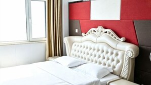 A neatly made bed with a white comforter and pillows, a cream-colored bedside table, and a red and white headboard. - Song Nantaiting Hotel (Junan County)