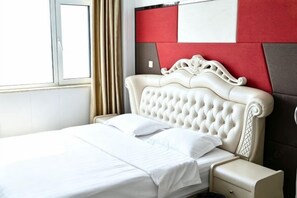A neatly made bed with a white comforter and pillows, a cream-colored bedside table, and a red and white headboard. - Song Nantaiting Hotel (Junan County)