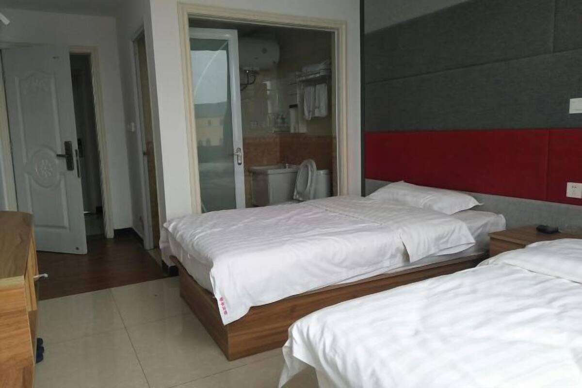 A hotel room with two beds, a wardrobe, and a bathroom visible through an open door.