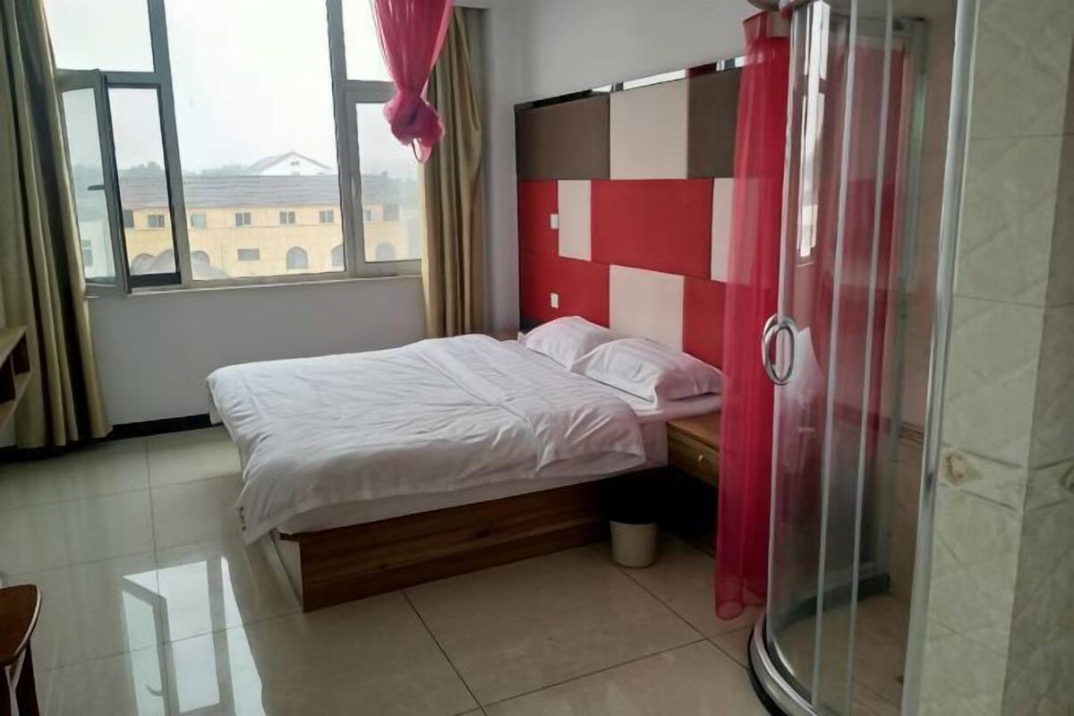 A hotel room with a bed, a shower, and a window with curtains.