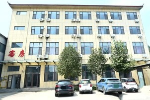 Un edificio de varios pisos con una fila de ventanas en la planta baja, un letrero con caracteres chinos y varios autos estacionados frente a él.