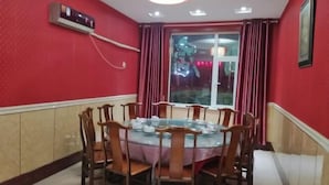 A dining area with a round table, chairs, a window with curtains, and a wall-mounted air conditioner. - Song Nantaiting Hotel (Junan County)