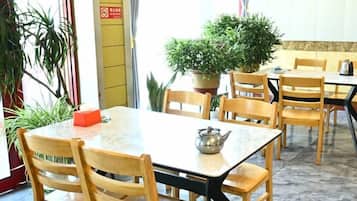 A dining area with wooden chairs and tables, potted plants, and a teapot on the table.