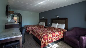 A room with two beds, a desk, and a purple armchair. - Excel Inn & Suites (Fredericksburg)