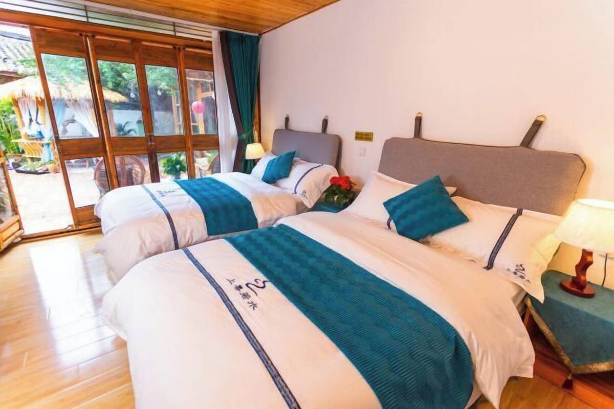 A hotel room with two beds, a wooden floor, a large window, and a view of the outdoors.