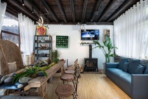 A cozy living room with a wooden bench, a sofa, and a fireplace. There are shelves with books and decorative items, and a television mounted on the wall. - Lijiang Shu He Shangshanruoshui Inn (Lijiang)