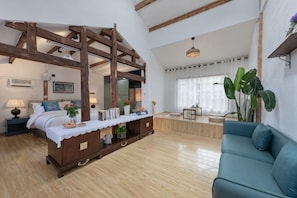 A bedroom with a wooden bed, a blue sofa, a dining table, and a large window.