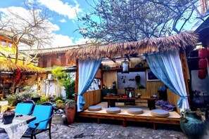 An outdoor seating area with a thatched roof, cushioned seating, and a wooden table. - Lijiang Shu He Shangshanruoshui Inn (Lijiang)