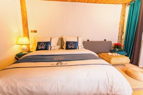 A neatly made bed with a blue and white bedspread, a bedside lamp, and a small table with a basket and flowers.