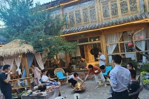 Un'area pranzo all'aperto con una struttura a tetto di paglia, tavoli imbanditi e persone che cenano.
