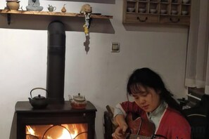 Una stanza con una stufa a legna, uno scaffale con servizi da tè e una poltrona.