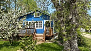 A blue house with a wooden staircase leading to the entrance, surrounded by lush greenery and trees.