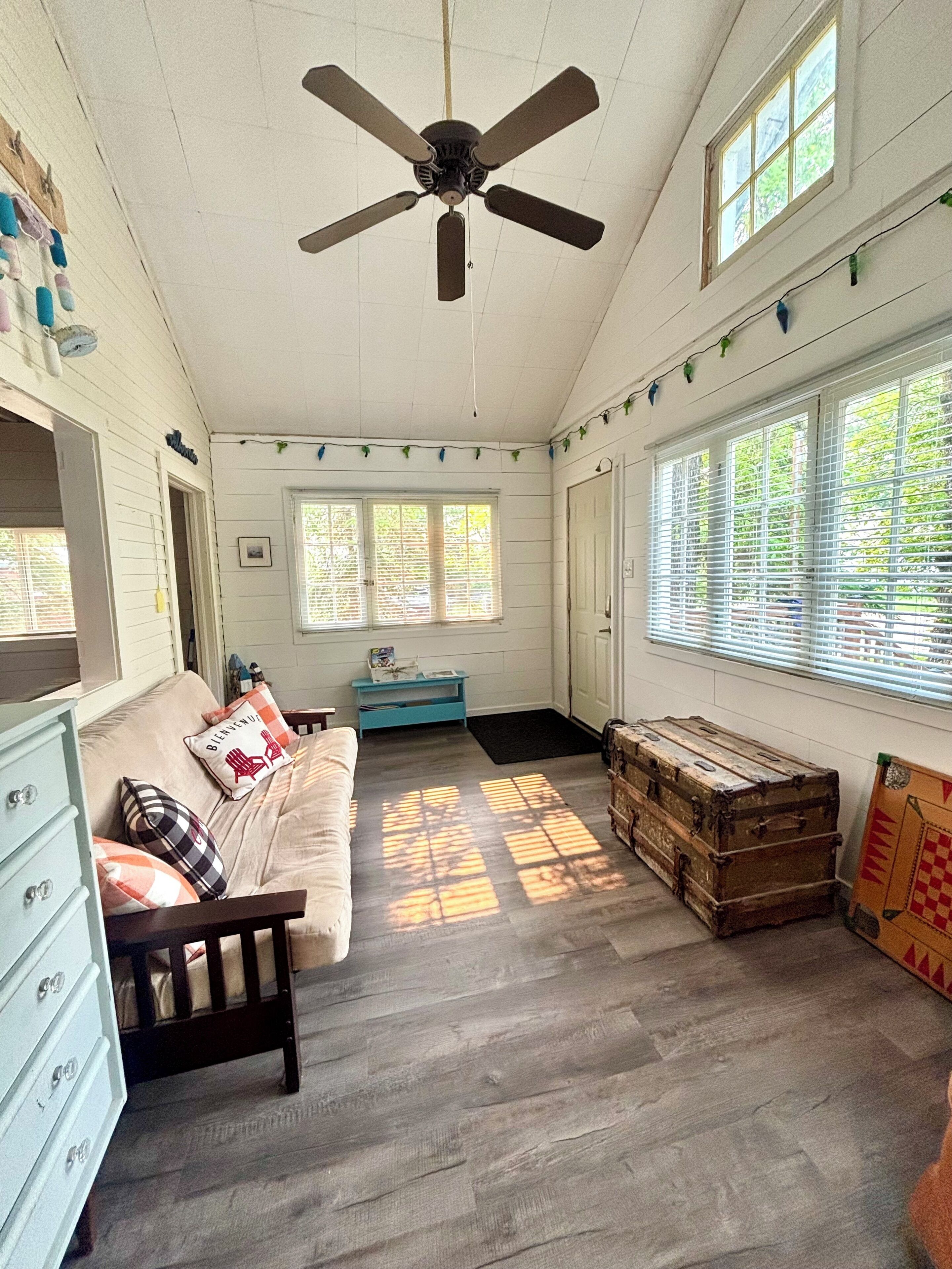 A room with a ceiling fan, a sofa, a dresser, a window with blinds, and a wooden chest.