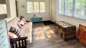 A room with a ceiling fan, a sofa, a dresser, a window with blinds, and a wooden chest.