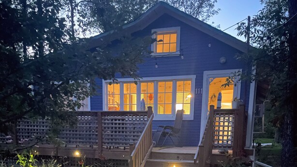 A house with a wooden deck leading to a front door, surrounded by a garden and trees.