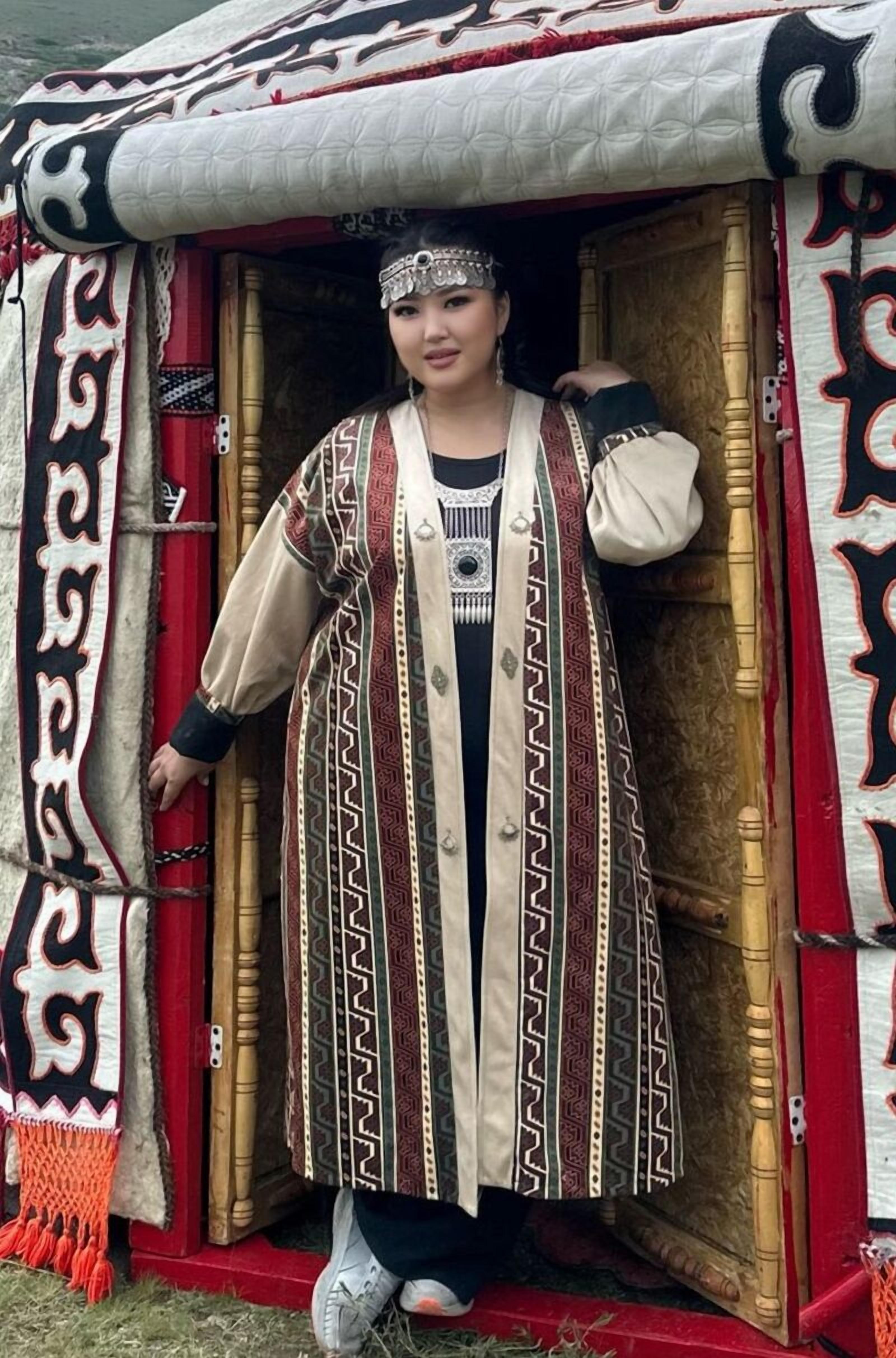 Une personne se tient devant une structure traditionnelle ornée de motifs complexes et aux couleurs rouge et blanc.