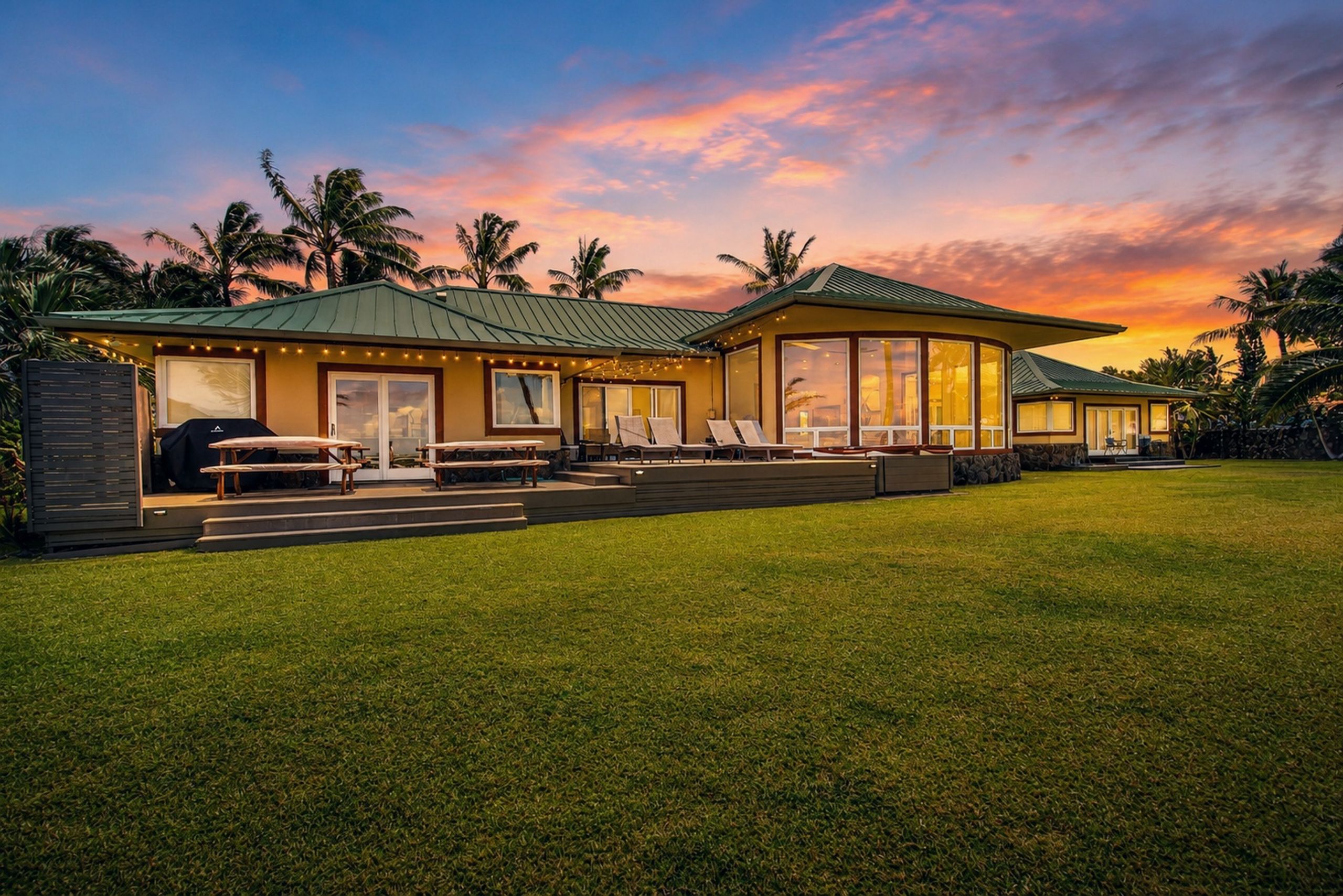 A modern house with a large deck, outdoor seating, and a view of the sunset.