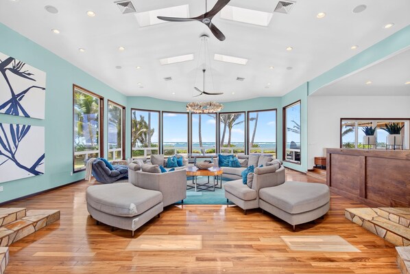 A spacious living room with a view of the ocean, large windows, and a ceiling fan.