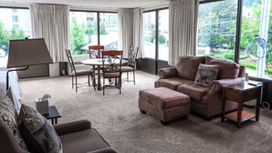 A spacious living room with a large window, a dining area, and a sofa with decorative pillows.