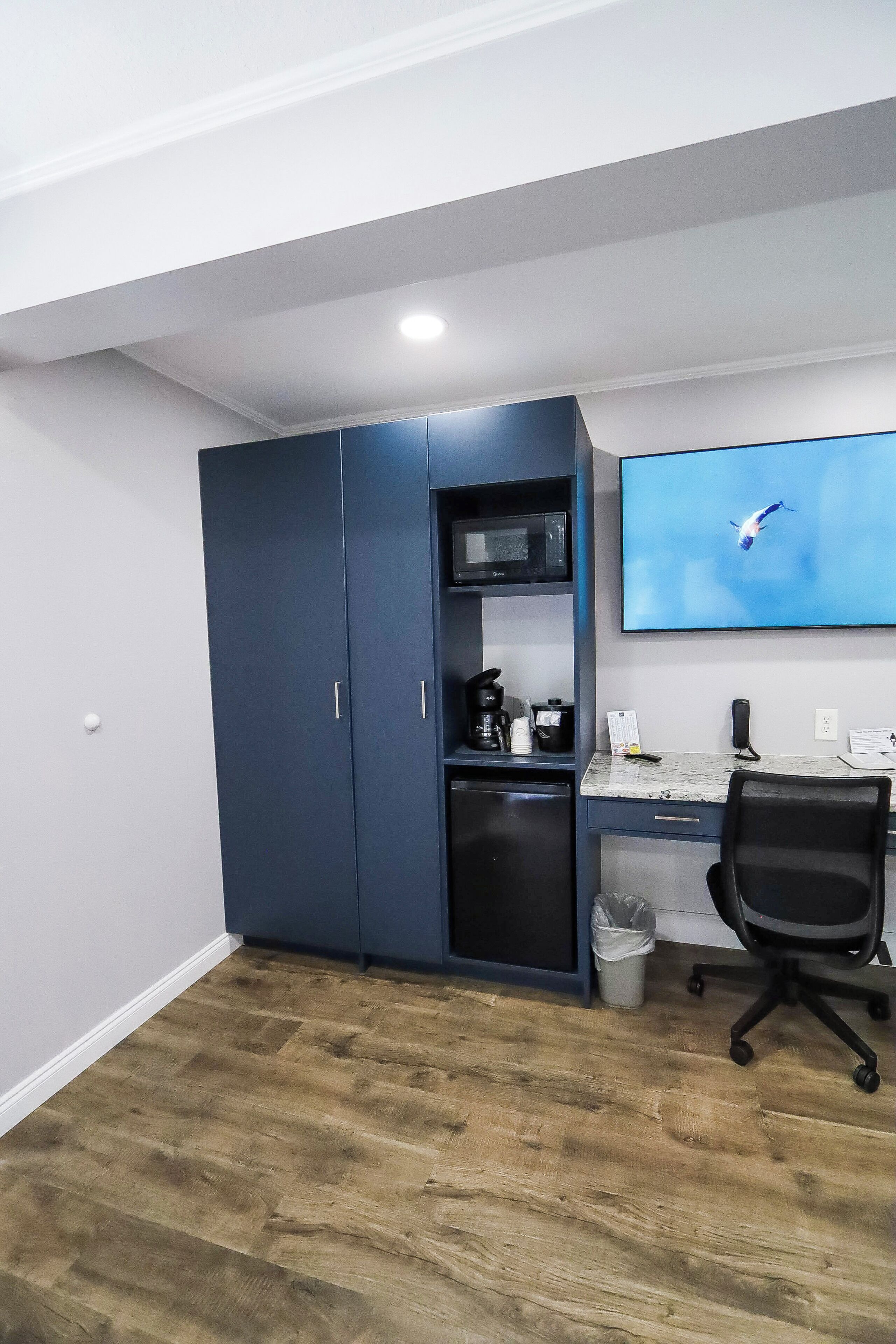 A room with a desk, a chair, a TV mounted on the wall, a microwave, and a cabinet.