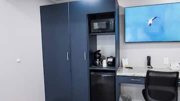 A room with a desk, a chair, a TV mounted on the wall, a microwave, and a cabinet.