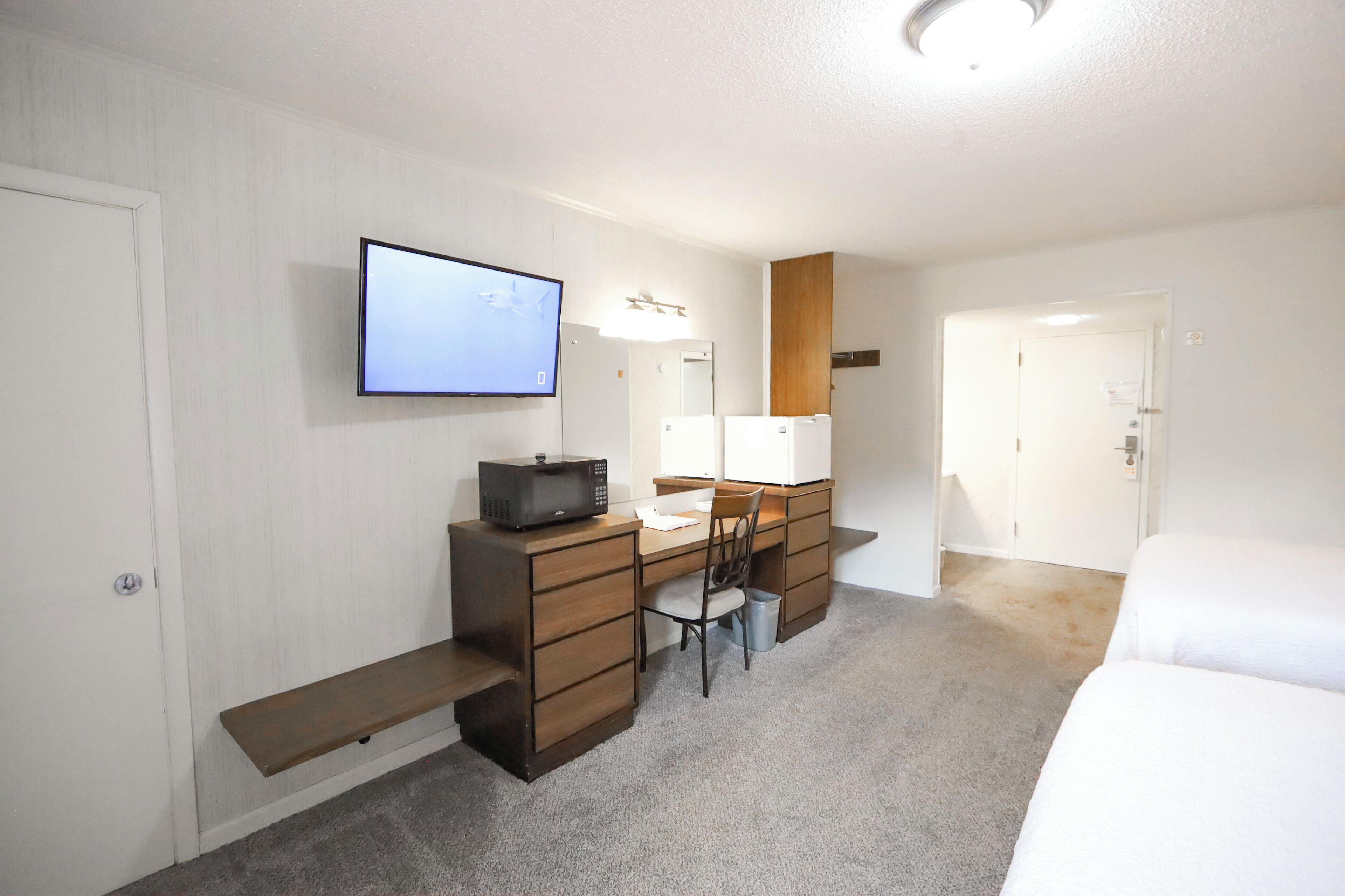 A hotel room with a desk, chair, microwave, and a TV mounted on the wall.