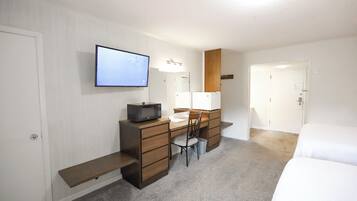 A hotel room with a desk, chair, microwave, and a TV mounted on the wall.