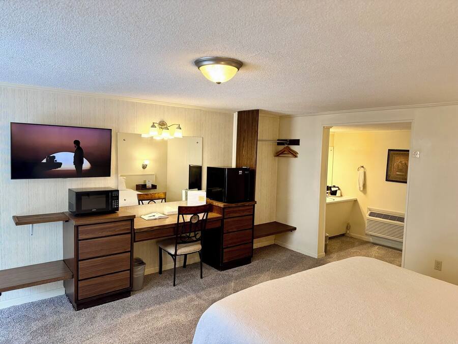 Une chambre d’hôtel comprenant un lit, un bureau avec un ordinateur, une télévision, un miroir et un luminaire fixé au mur.