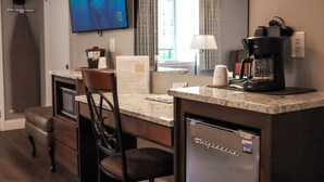A compact kitchen with a refrigerator, a coffee maker, a TV, and a dining area with a chair and table.