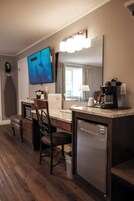 A compact kitchen with a refrigerator, a coffee maker, a television, and a dining area with a chair and table.