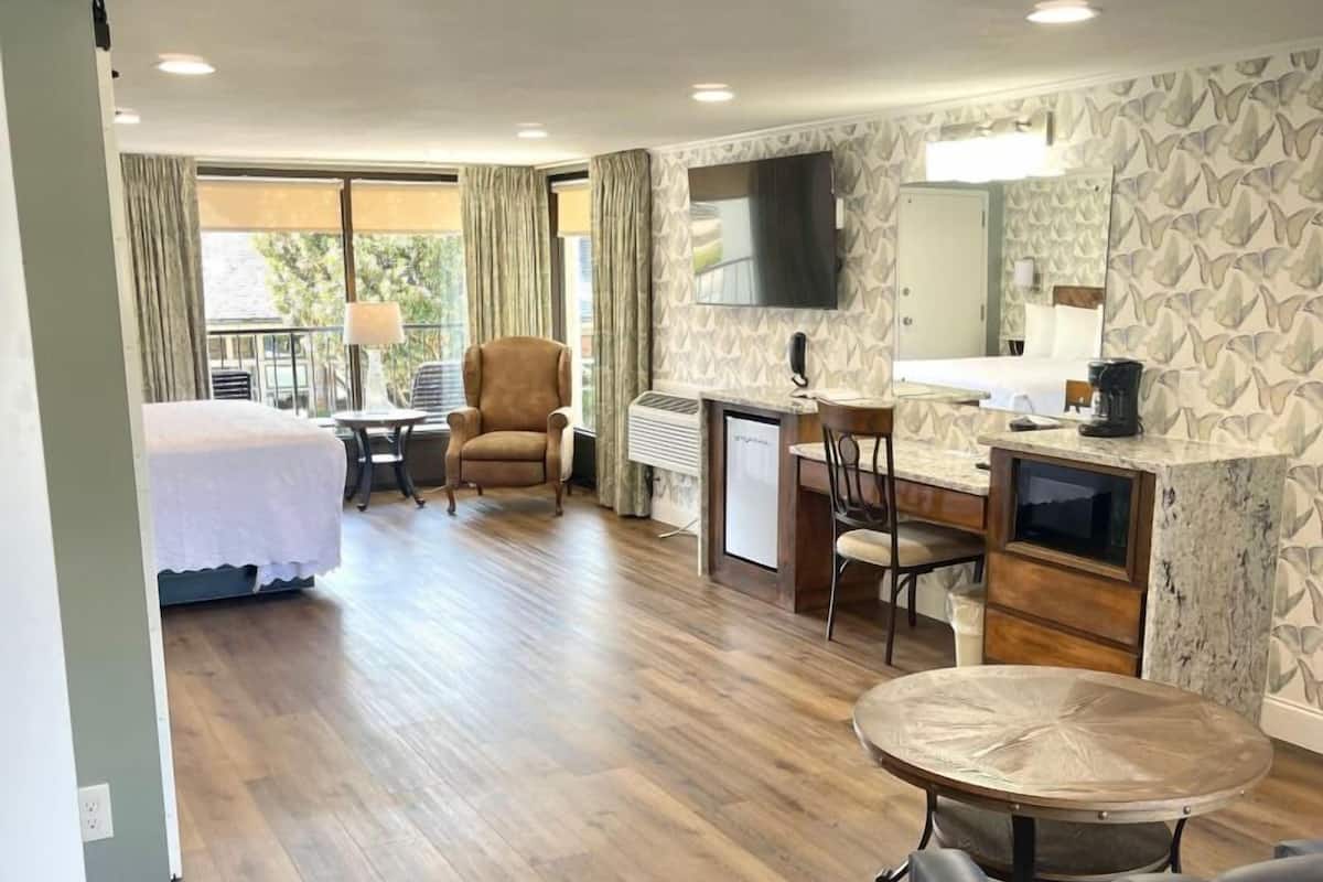 Habitación de hotel con cama, escritorio, silla, televisor y balcón con cortinas.