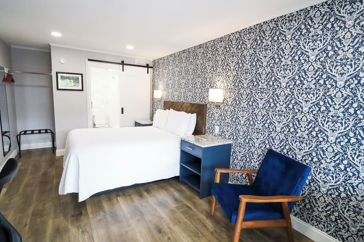 Un dormitorio con cama, escritorio y silla, un papel tapiz decorado en la pared y una puerta.