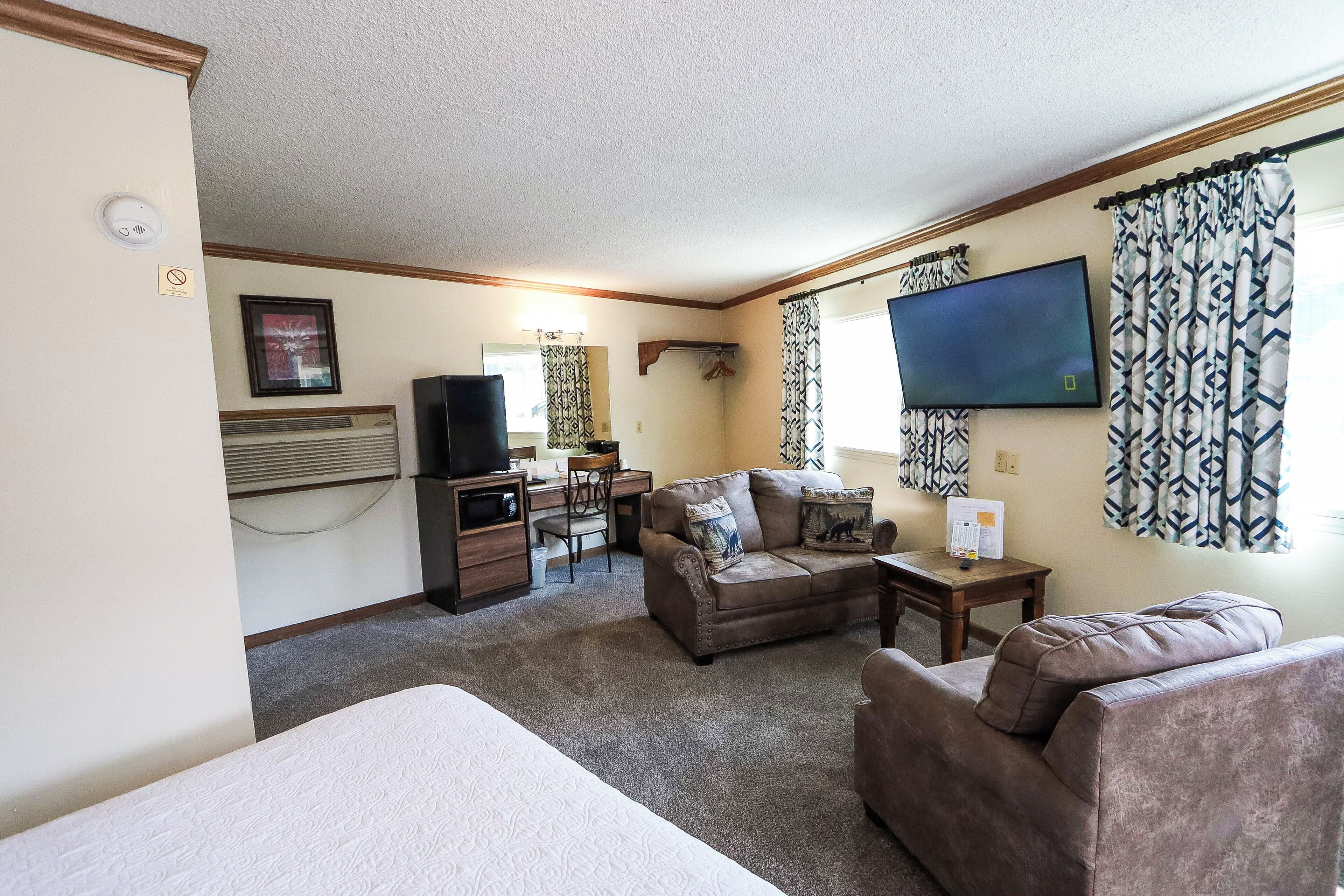 A furnished living room with a sofa, armchair, and a flat-screen TV mounted on the wall.