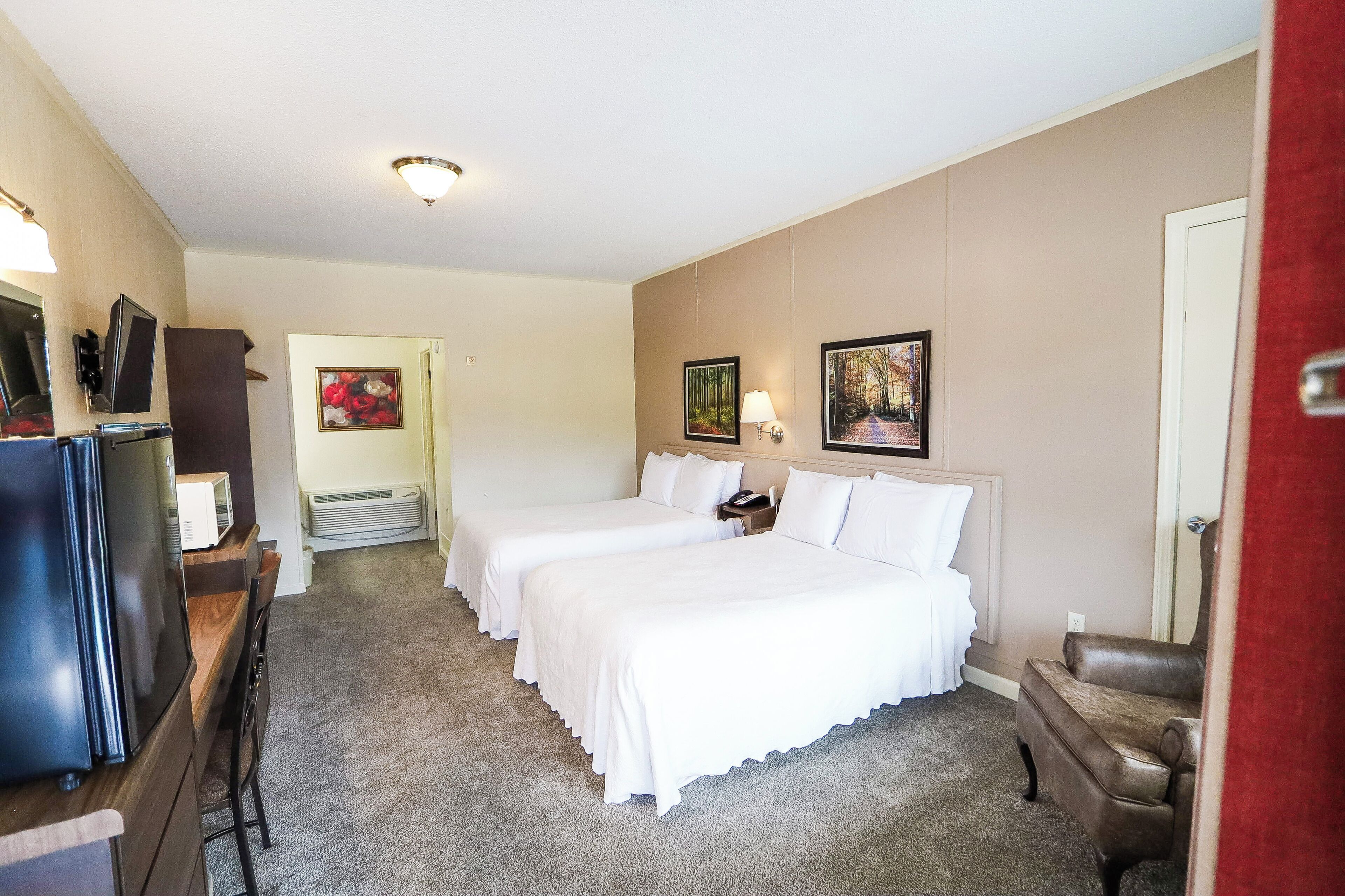 A hotel room with two beds, a TV, a desk, and a chair.