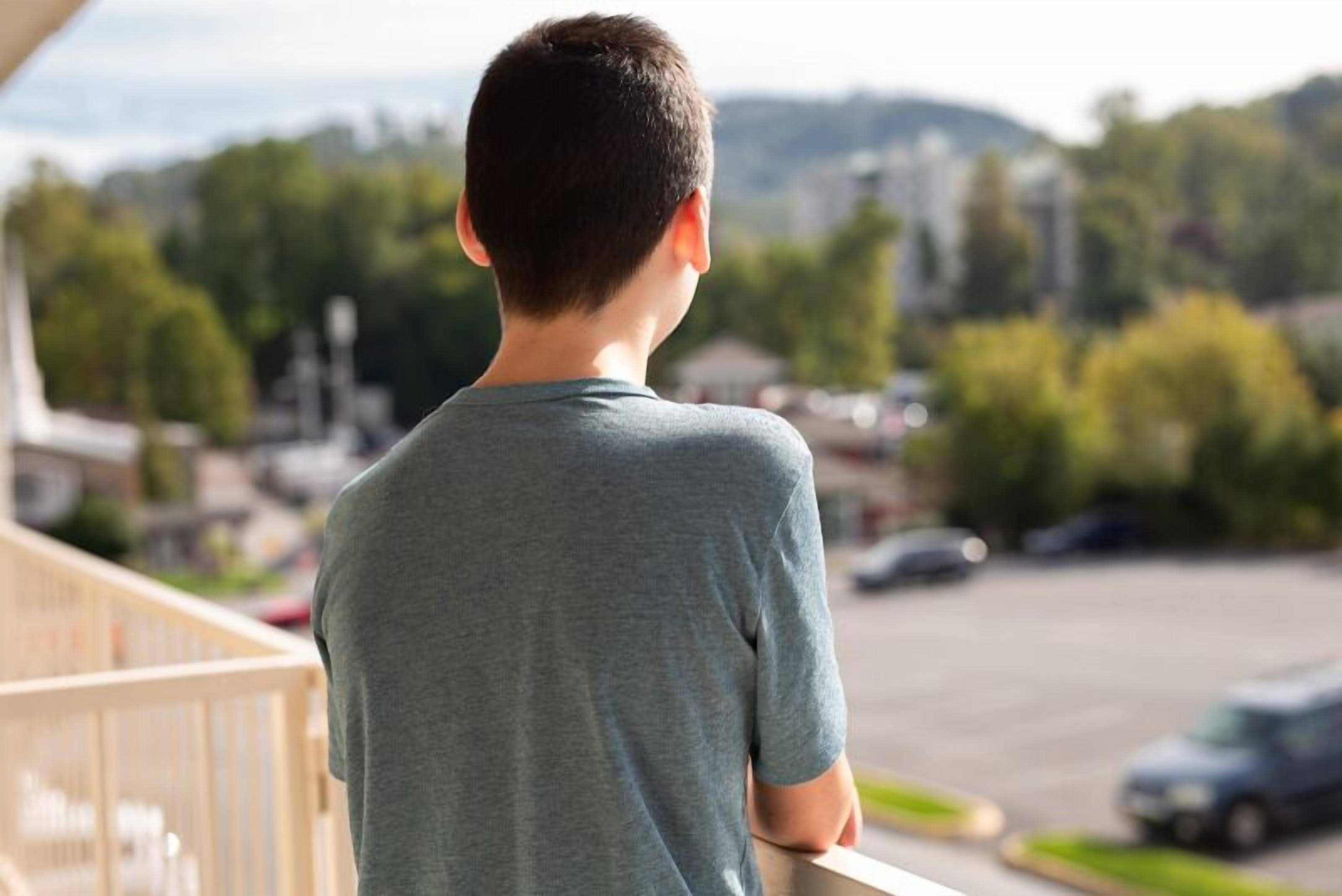 A person standing on a balcony overlooking a parking lot and greenery.