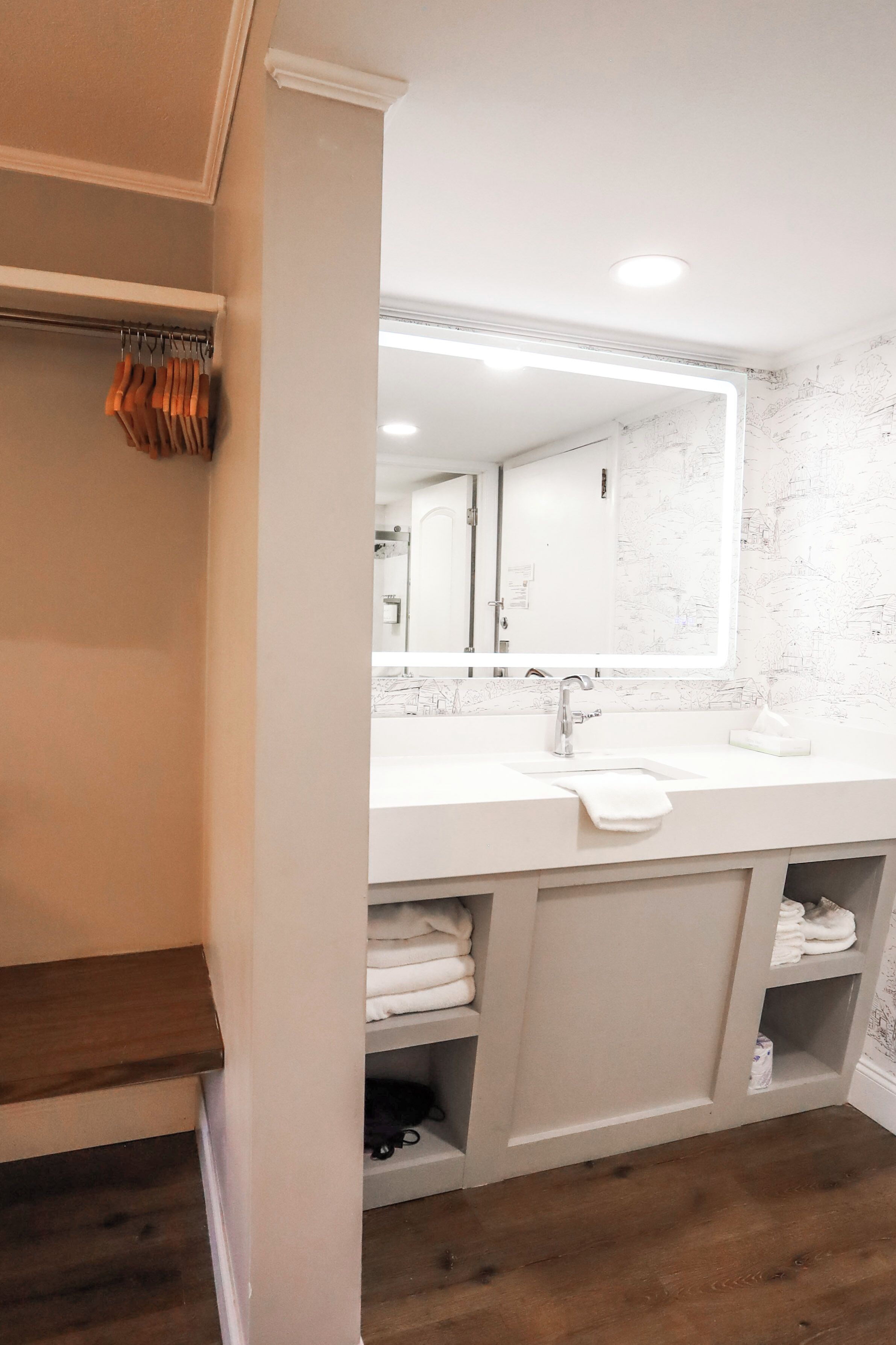 Une salle de bain avec un lavabo blanc, un miroir et un plancher en bois.
