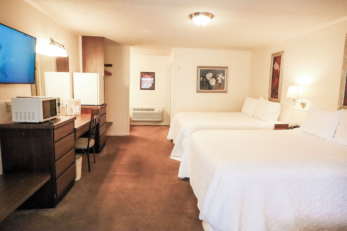 Habitación de hotel con dos camas, un escritorio con microondas, un televisor y un aparador.