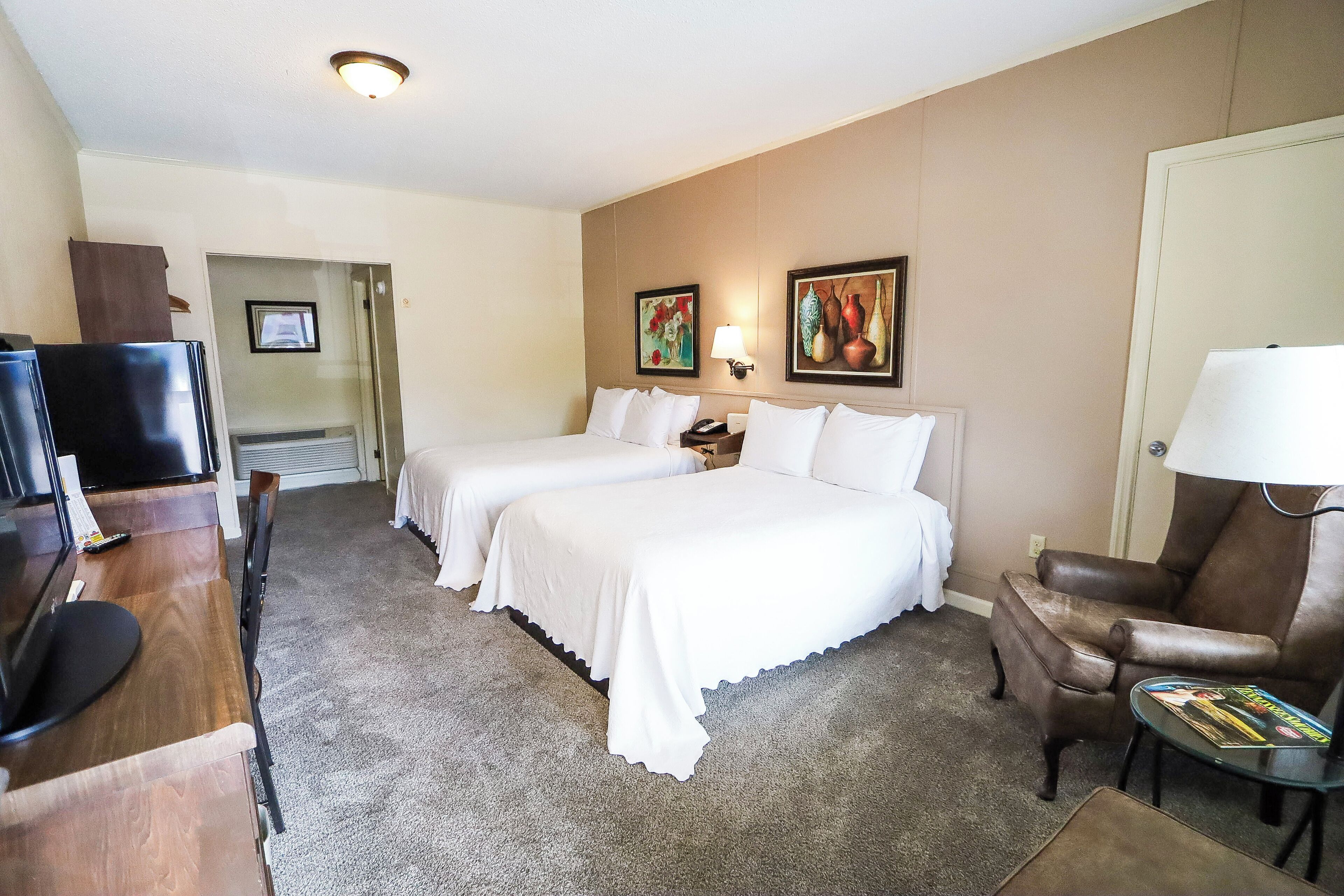 A hotel room with two beds, a desk with a TV, a chair, and a lamp.