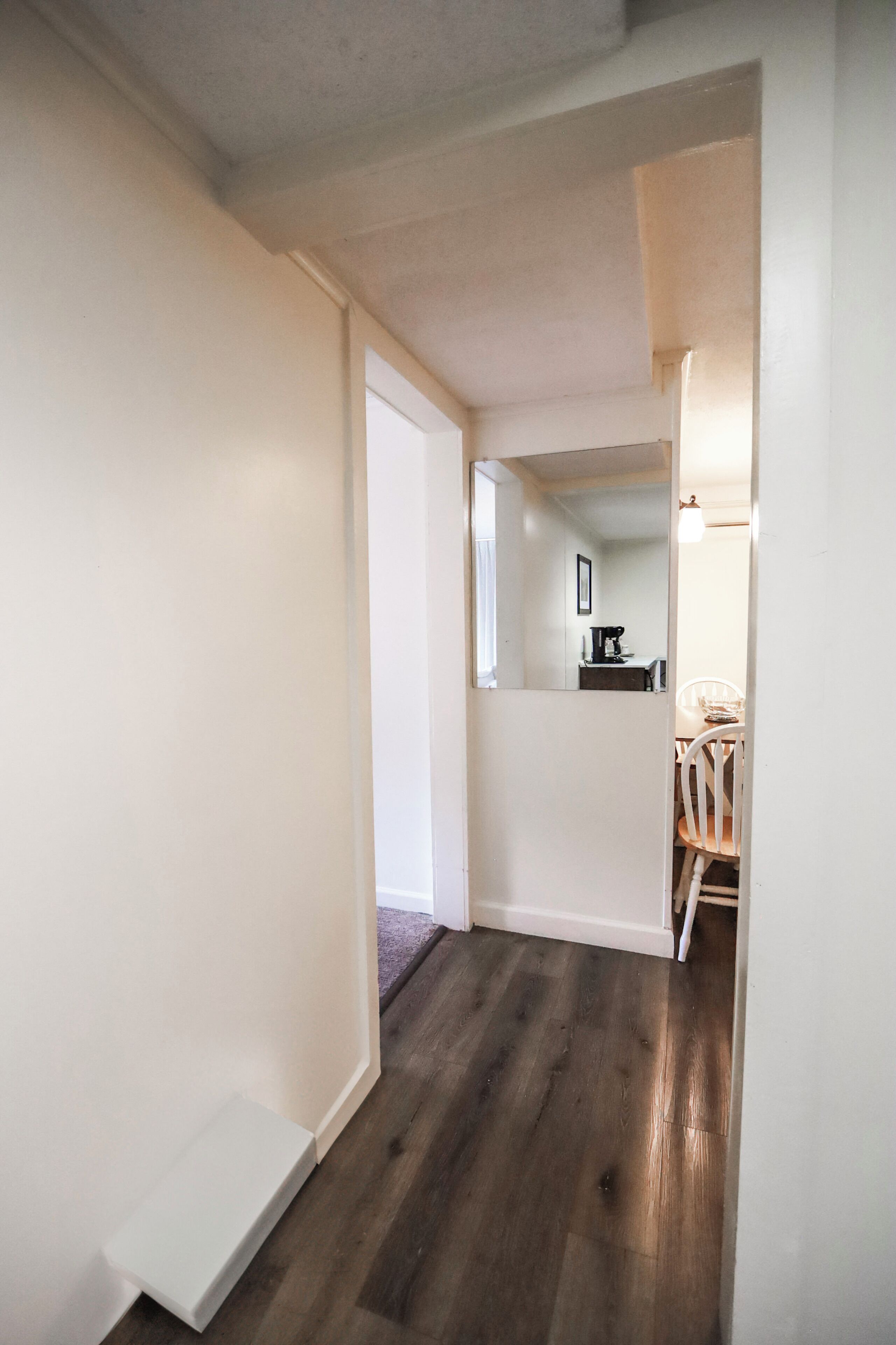 A hallway with a wooden floor leading to a dining area with a white chair and a table.