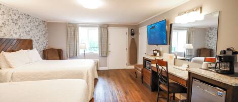 A hotel room with two beds, a desk with a chair, a refrigerator, a television, and a window with curtains.