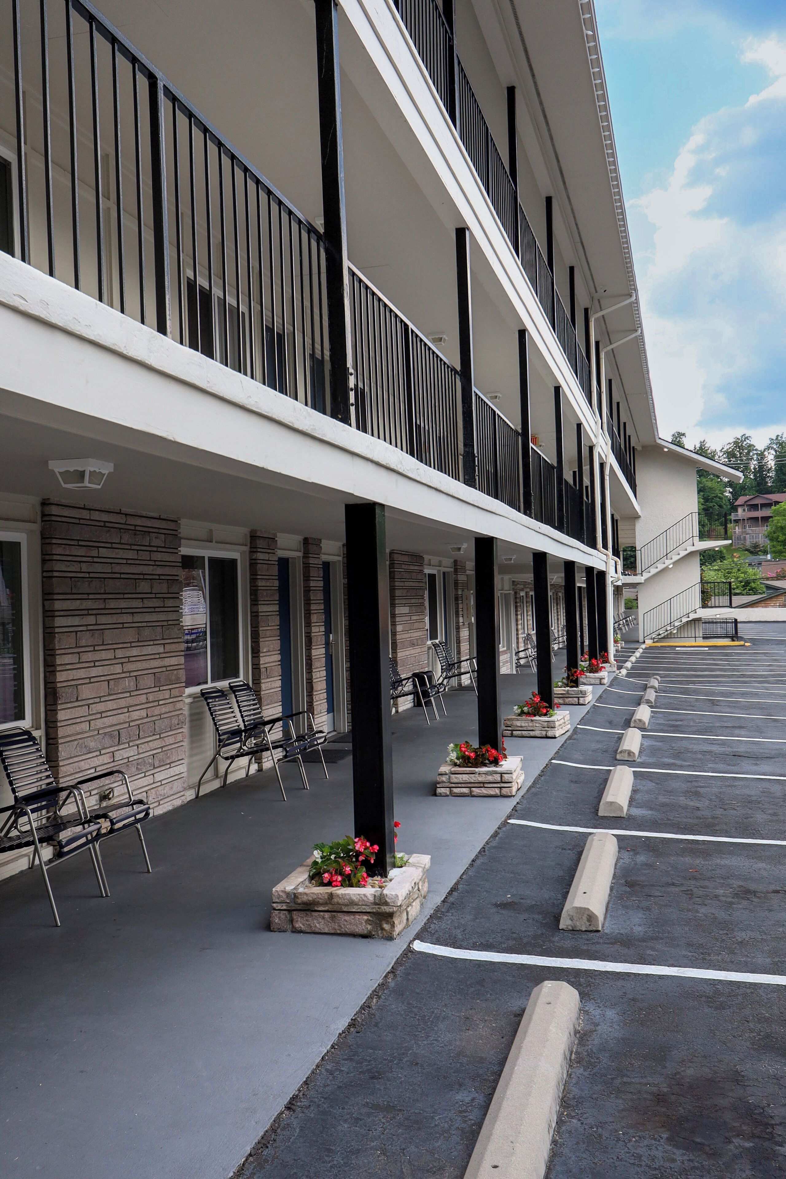 A hotel with a covered outdoor seating area, multiple balconies, and a parking lot.