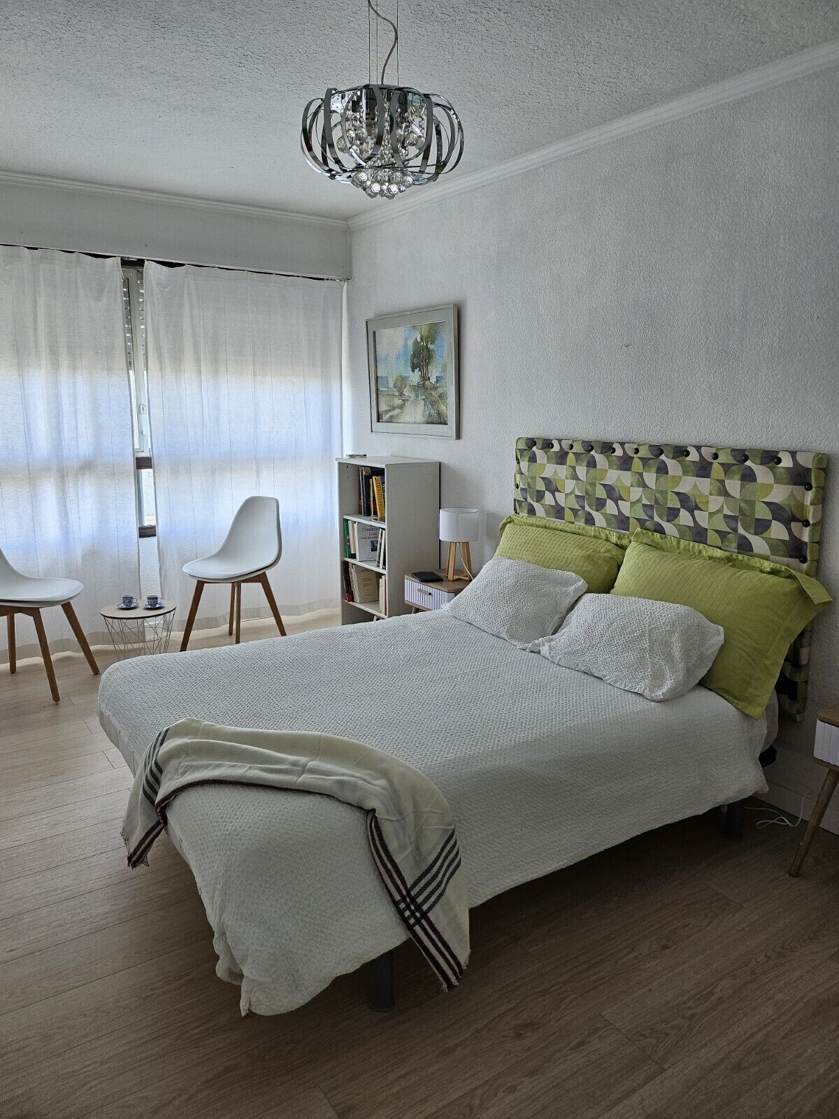 Une chambre à coucher avec un lit, un lustre, une bibliothèque et un tableau accroché au mur.