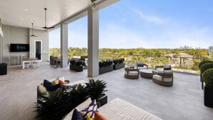 A spacious outdoor area with modern seating, a ceiling fan, and a view of the cityscape.